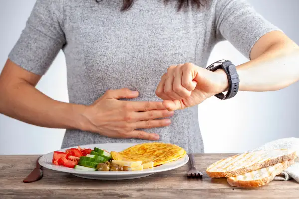 Intermittent Fasting: A Personal And Scientific Perspective A person checking their watch while sitting in front of a healthy meal, emphasizing the importance of meal timing and regular eating schedules for digestive health