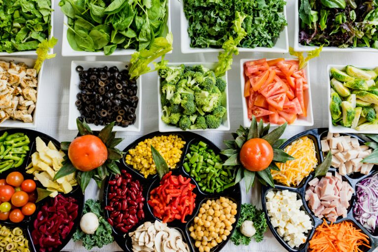 An array of colourful, fresh vegetables including spinach, kale, broccoli, tomatoes, bell peppers, corn, chickpeas, olives, and more displayed in bowls and platters, representing a nutritious and balanced diet for boosting immune health.