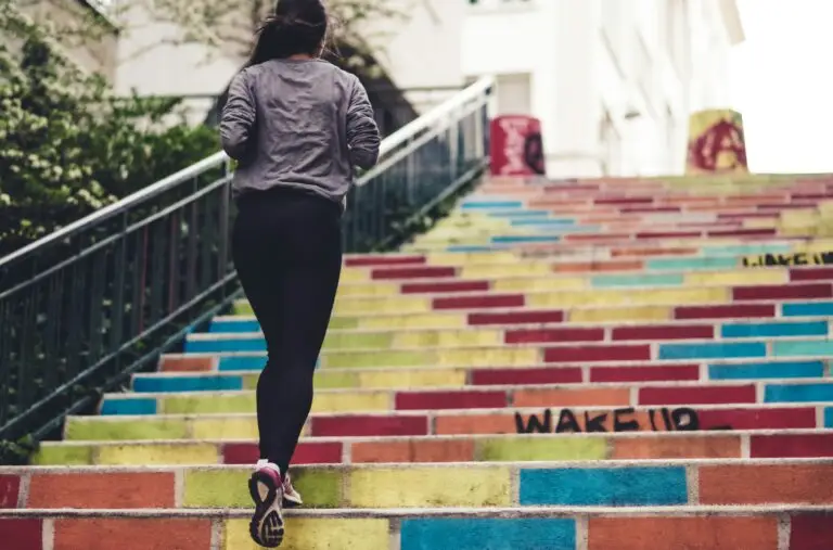 Unlock The Secret Doctors Won’t Tell You: The Ultimate Guide To Defeating Diabetes In No Time! A woman in athletic clothing running up a set of colourful outdoor stairs, with greenery on the side and buildings in the background.