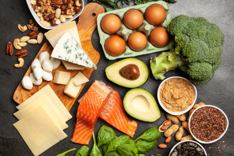 Healthy foods rich in saturated fats including cheese, salmon, avocado, eggs, nuts, broccoli, and leafy greens.