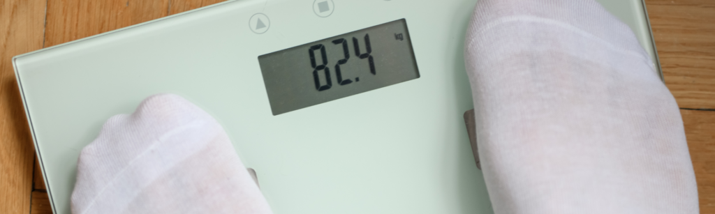 Person standing on a digital scale showing 82.4 kg